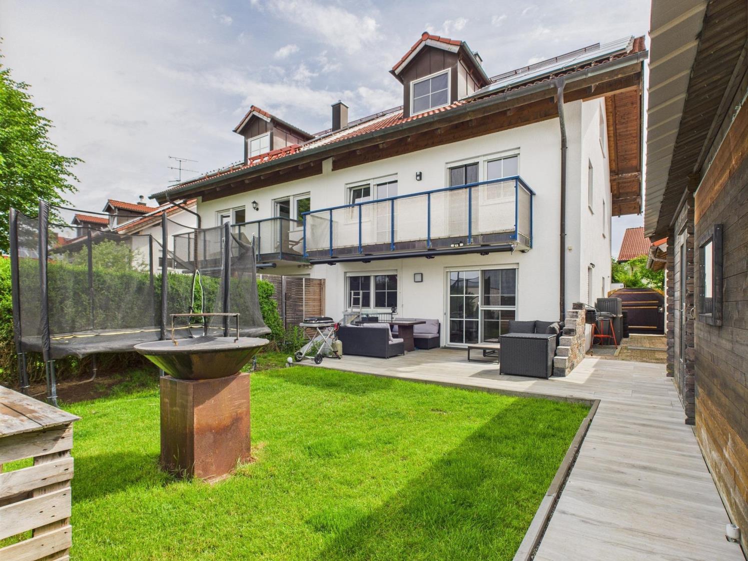 Doppelhaushälfte mit hellem Putz, rotem Satteldach, Balkon und gepflegtem Garten mit Terrasse und Spielbereich.